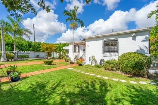 6851 SW 32nd Street, Miami, FL 33155 Exterior grounds featuring a manicured lawn, brick-paved pathways, circular stone stepping stones, perimeter privacy fencing, and mature palm trees