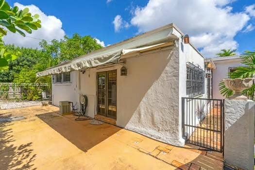 6851 SW 32nd Street, Miami, FL 33155 Stucco exterior featuring a retractable awning, glass-paneled double doors, metal security window bars, and a paved patio area