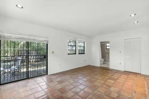 6851 SW 32nd Street, Miami, FL 33155 Spacious room featuring terra-cotta tile flooring, recessed lighting, white louvered closet doors, and a sliding glass door with integrated security bars