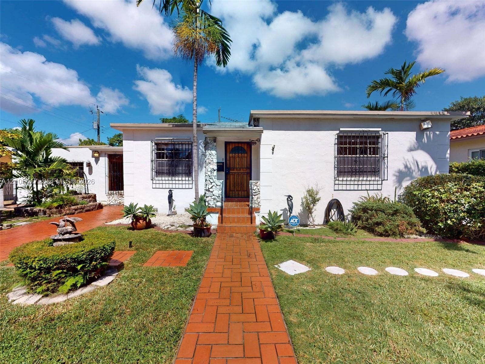 6851 SW 32nd Street, Miami, FL 33155 Single-story exterior featuring white stucco finish, red brick paver walkway, stone-accented entryway, and metal window security bars