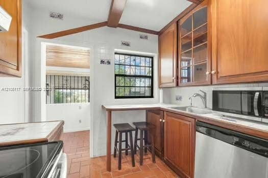 6851 SW 32nd Street, Miami, FL 33155 Kitchen featuring wood cabinetry with glass-panel upper doors, integrated breakfast bar, stainless steel dishwasher, built-in microwave, and terracotta tile flooring