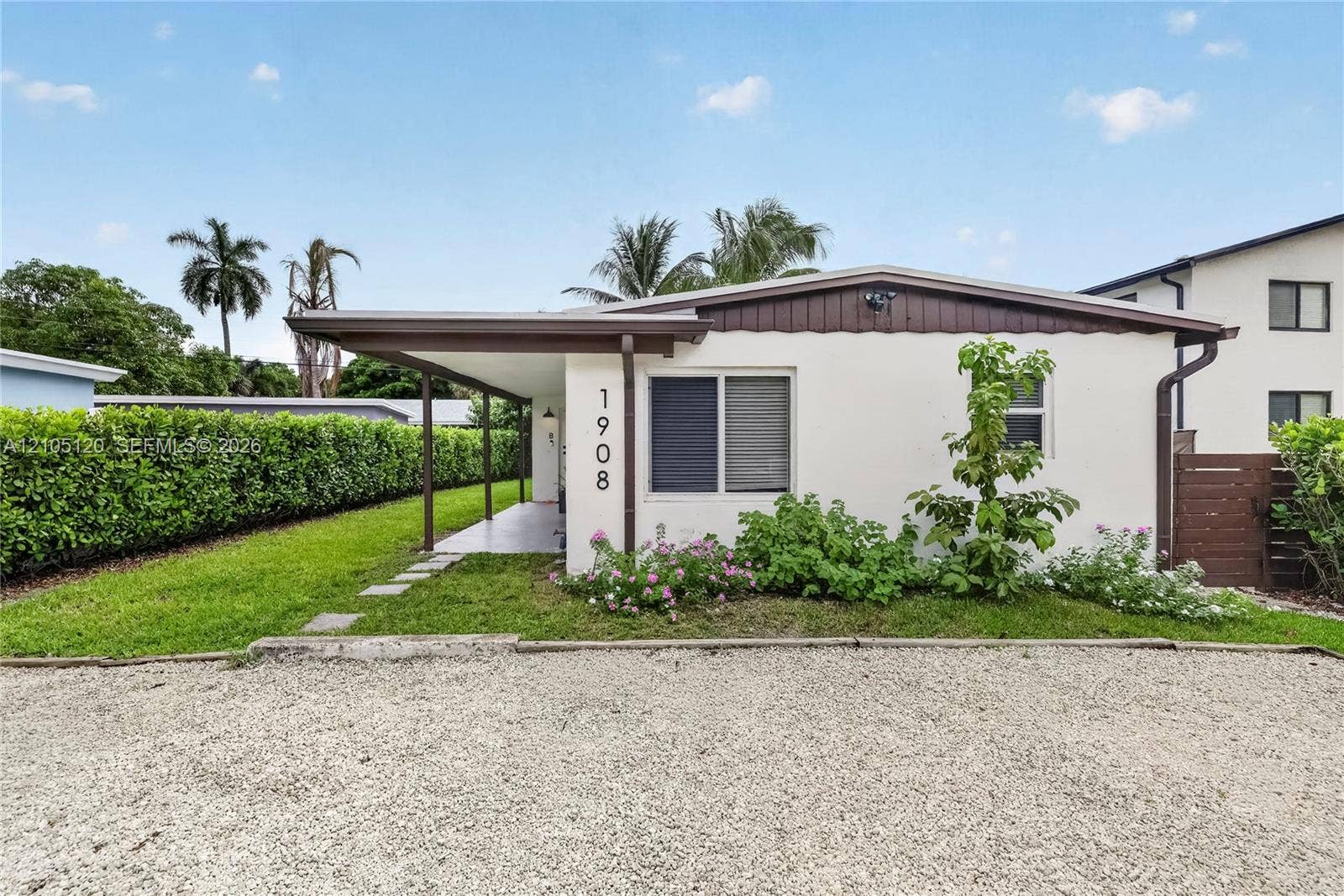 Fort Lauderdale, Fort Lauderdale, FL 33315 Exterior featuring a stucco facade, covered porch, gravel driveway, and landscaped perimeter with mature hedging