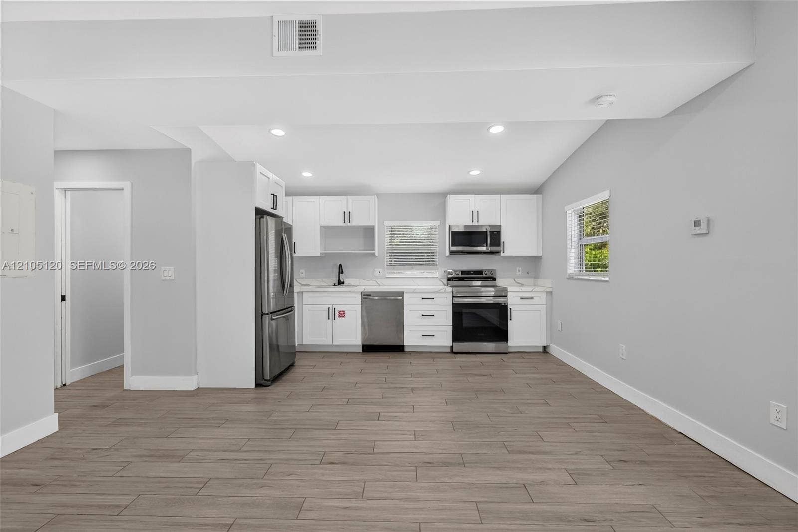 Fort Lauderdale, Fort Lauderdale, FL 33315 Kitchen featuring white shaker-style cabinetry, wood-finish flooring, recessed lighting, and stainless steel appliances including a microwave, dishwasher, and stove