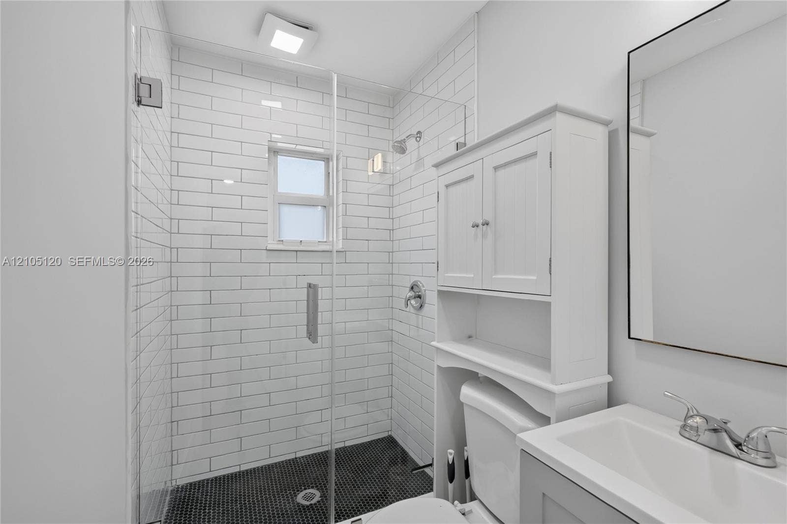 Fort Lauderdale, Fort Lauderdale, FL 33315 Walk-in shower with white subway tile surround, dark penny tile flooring, and a frameless glass door, accompanied by a white vanity with an integrated sink and an over-the-toilet storage cabinet