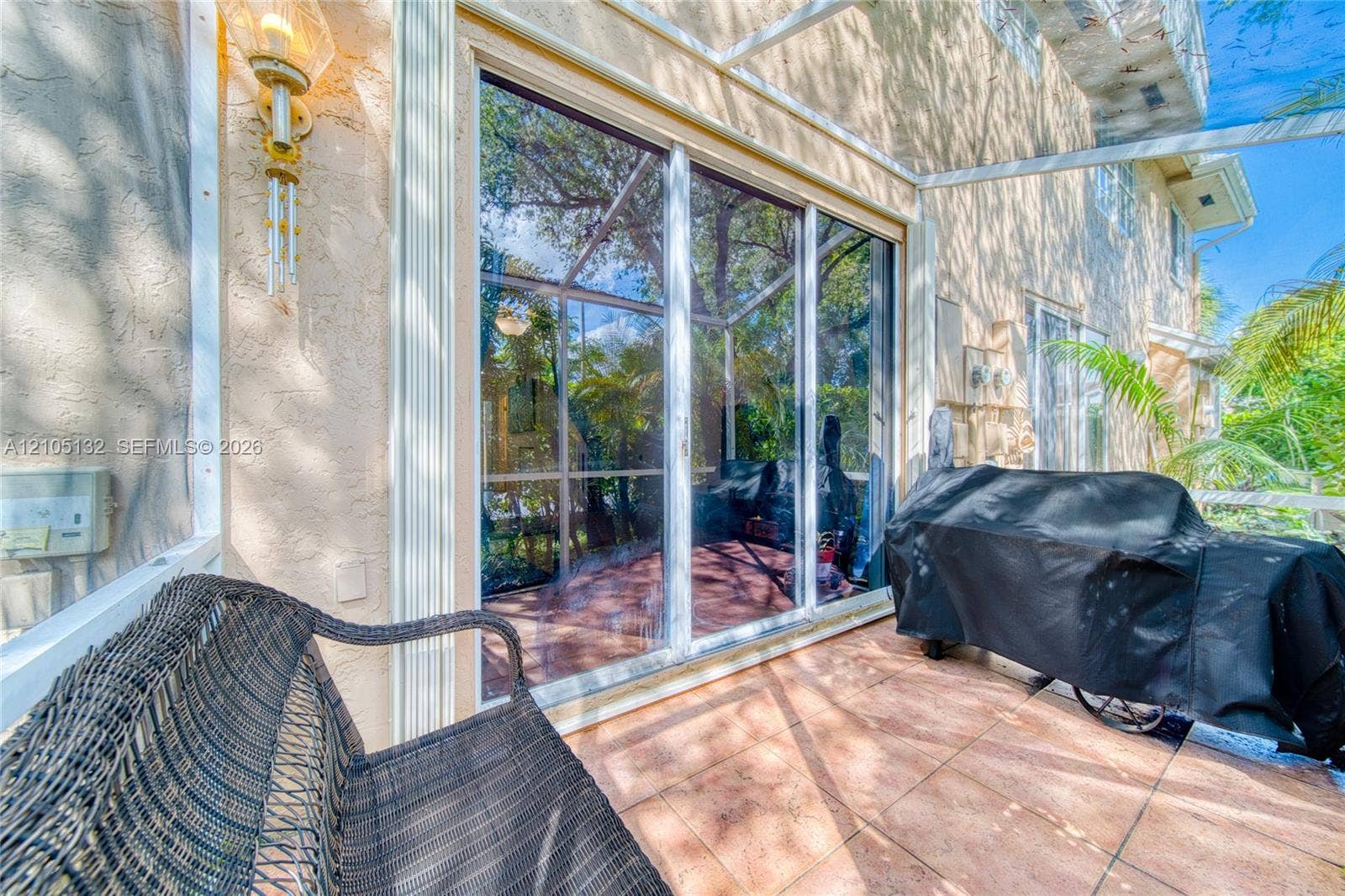 Expansive sliding glass doors, textured exterior wall, exterior wall sconce, and tiled patio flooring