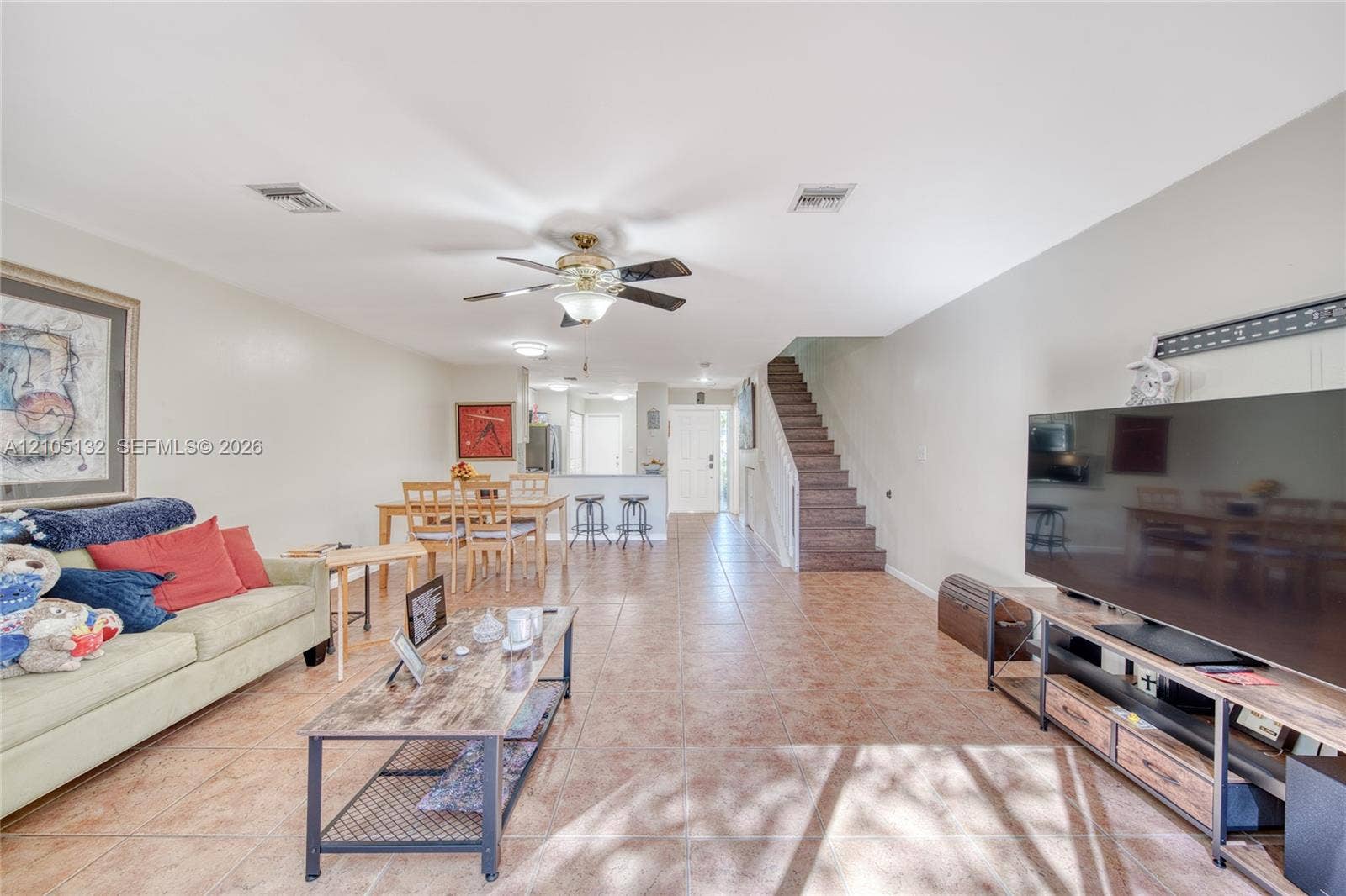 Open concept living area with tile flooring, ceiling fan, and stairwell with wood-finish treads