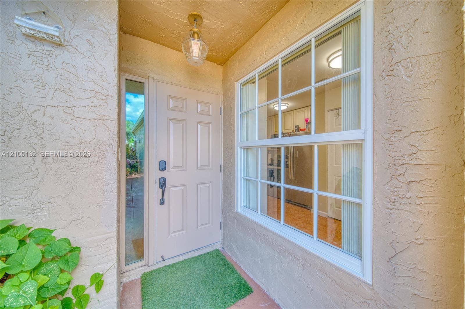 Textured stucco exterior, panel-style entry door, clear glass sidelight, exterior wall-mounted light fixture, and gridded window