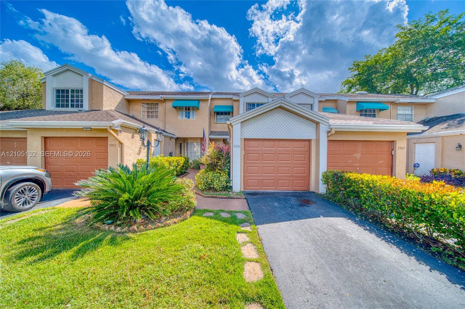 Multi-unit structure featuring stucco exterior, individual garage doors, paved driveways, and established landscaping