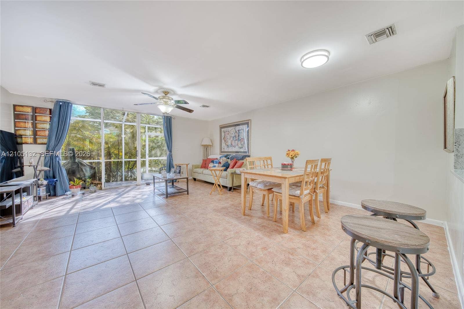 Tiled flooring throughout, featuring a dining area, a ceiling fan with integrated lighting, and a large window wall