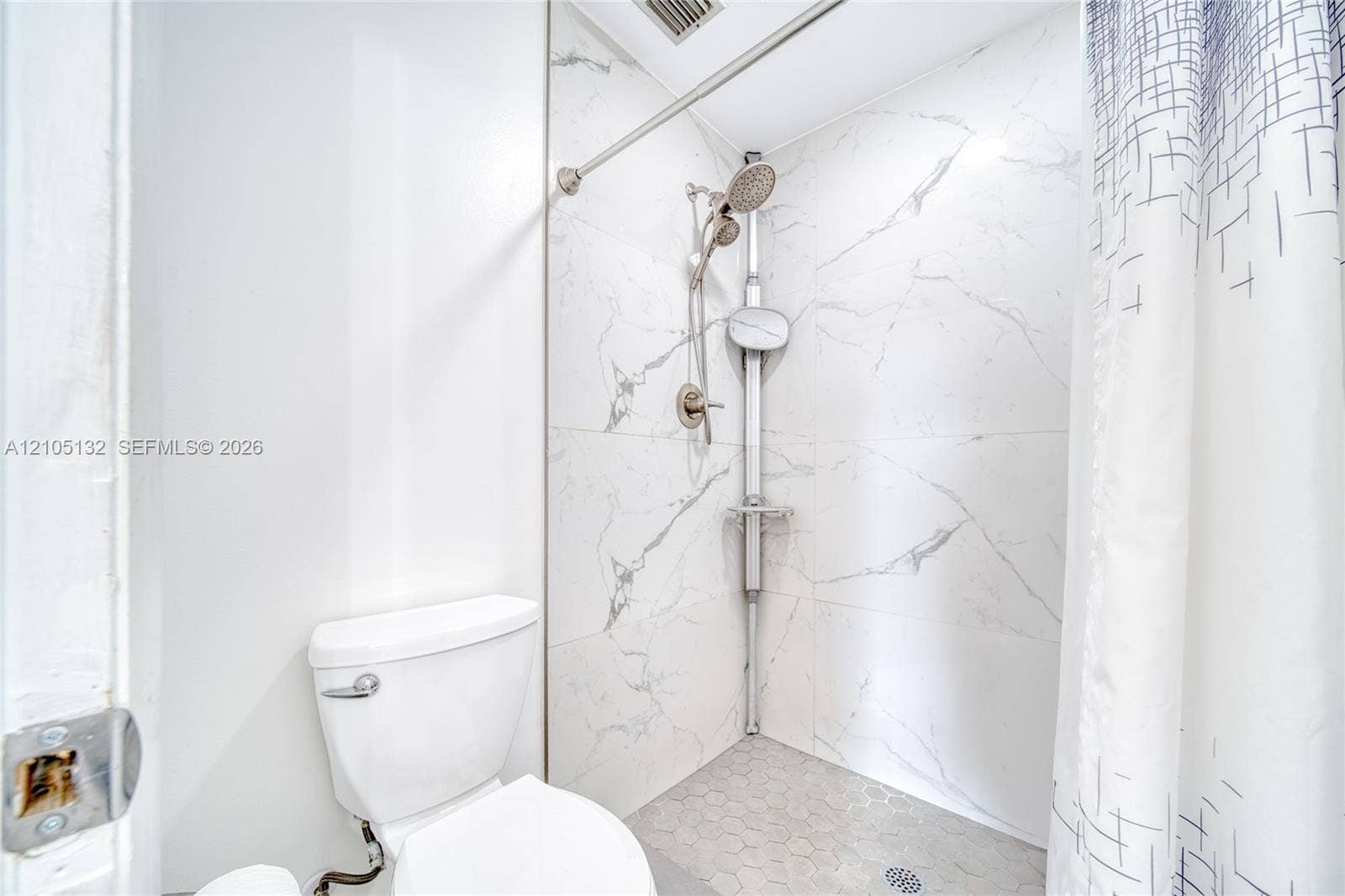 Walk-in shower with marble-finish wall tiling, hexagon-patterned floor tiling, and a brushed nickel shower system