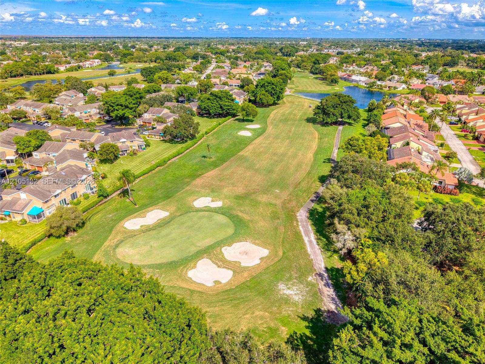 Expansive golf course setting with multiple sand traps, surrounded by residential properties, lush green landscaping, and natural water features