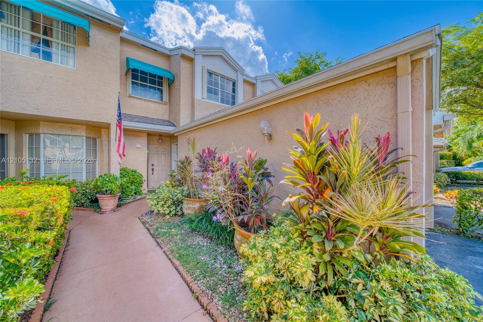 Stucco exterior, covered entry, front walkway, established landscaping, and window awnings