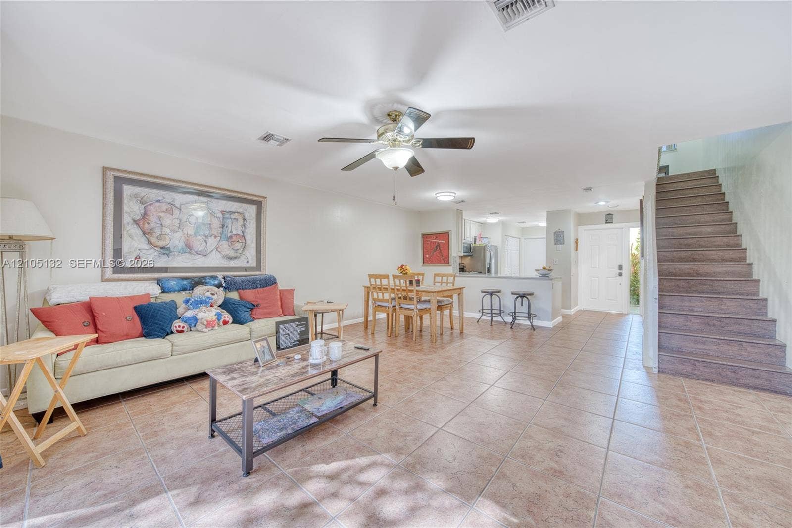 Open-concept living area with tile flooring, a ceiling fan, and a breakfast bar