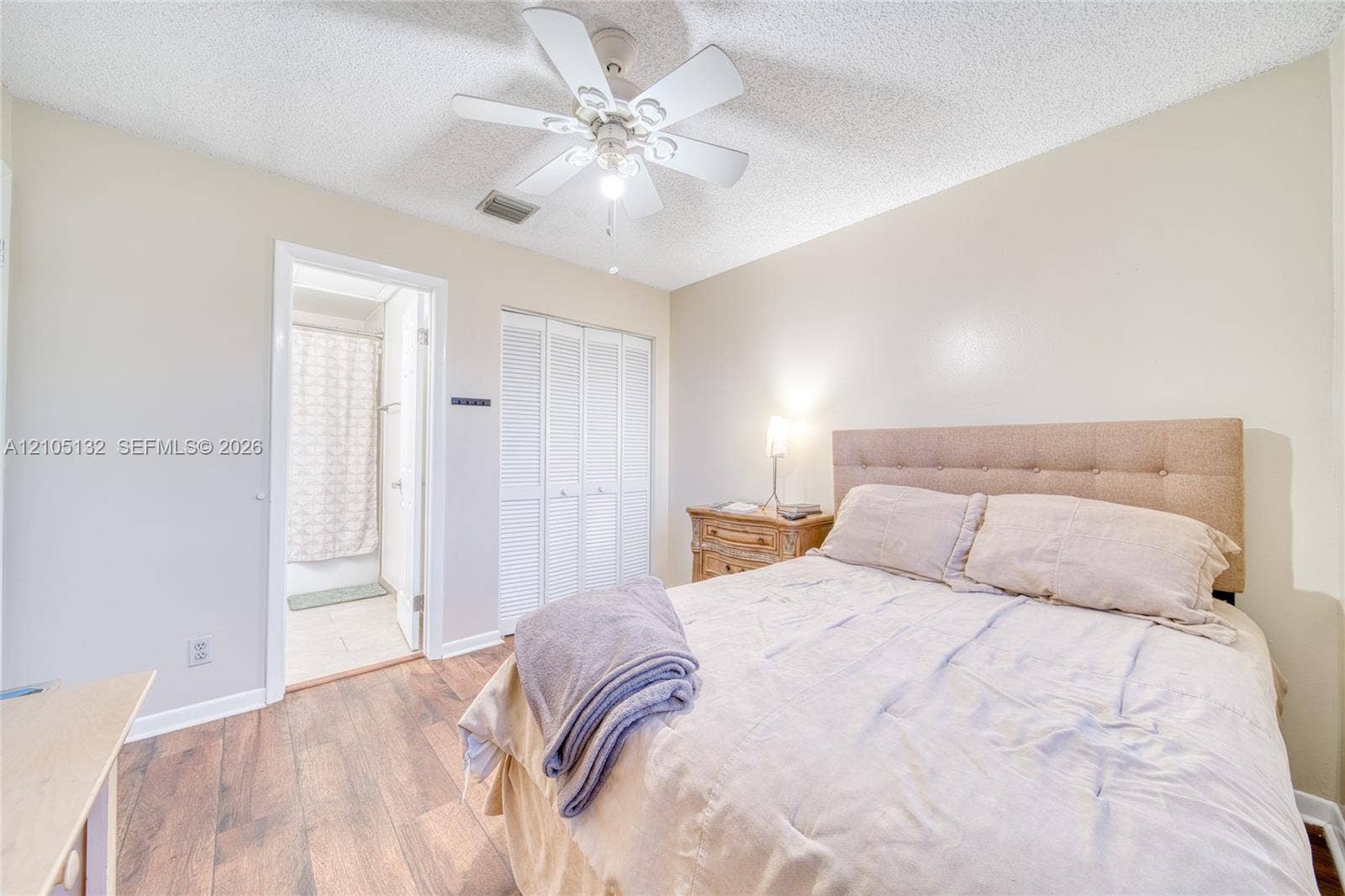 Wood-finish flooring, ceiling fan with light fixture, built-in closet with louvered doors, and light-toned walls