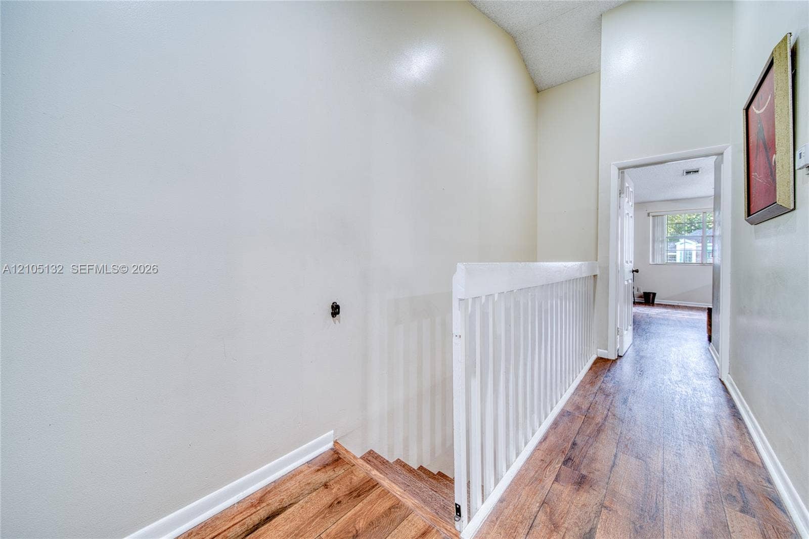 Wood-finish flooring throughout the hallway and staircase, white painted walls, and white painted stair railing