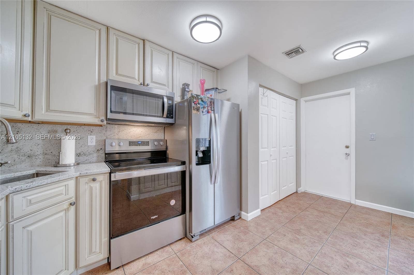 Kitchen featuring stainless steel appliances, light cabinetry, stone countertops, and tile flooring