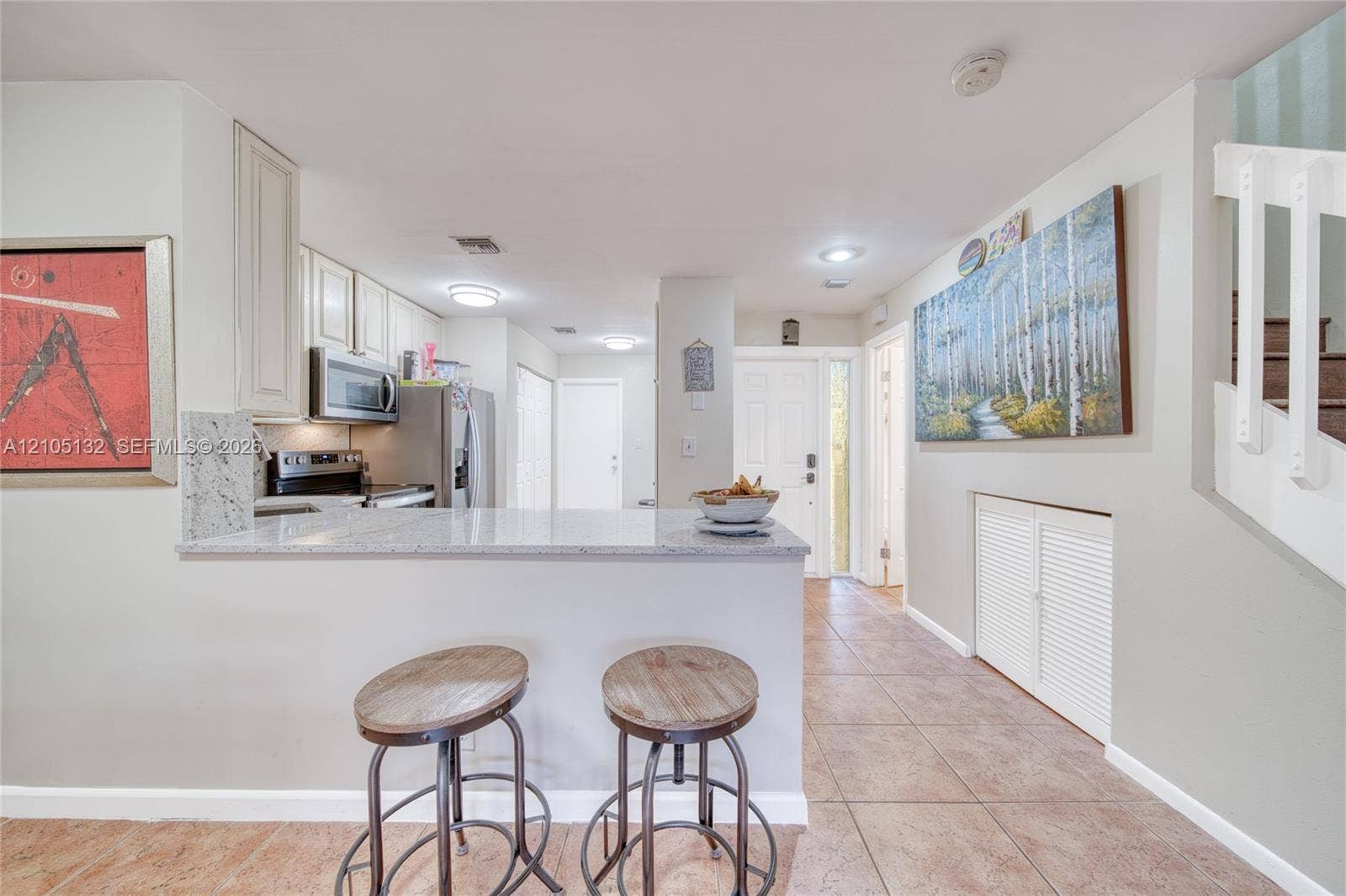 Kitchen pass-through with a light-toned countertop, white cabinetry, stainless steel appliances, and tile flooring