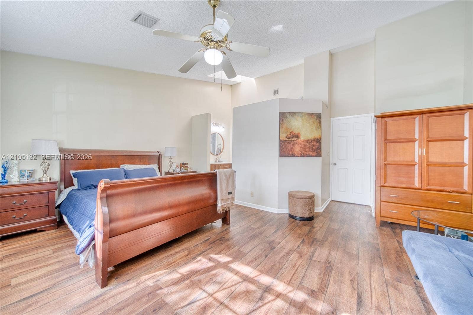 Wood-finish flooring throughout, ceiling fan with integrated lighting, vaulted ceiling, built-in vanity with mirror, and paneled interior door