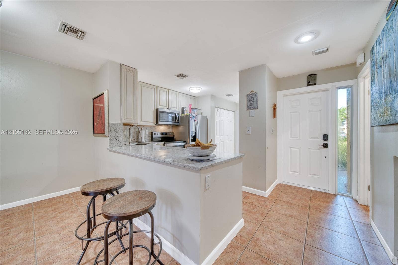 Kitchen island with a granite countertop, white paneled cabinetry, stainless steel appliances, and tile flooring