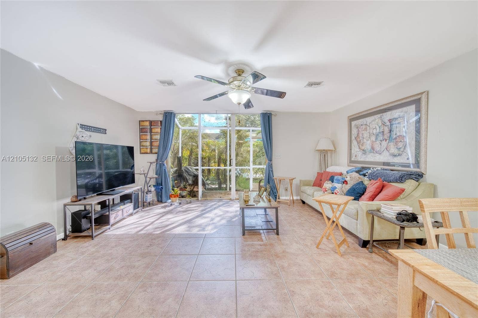 Expansive living area with large format tile flooring, ceiling fan with integrated lighting, and direct access to an enclosed outdoor space