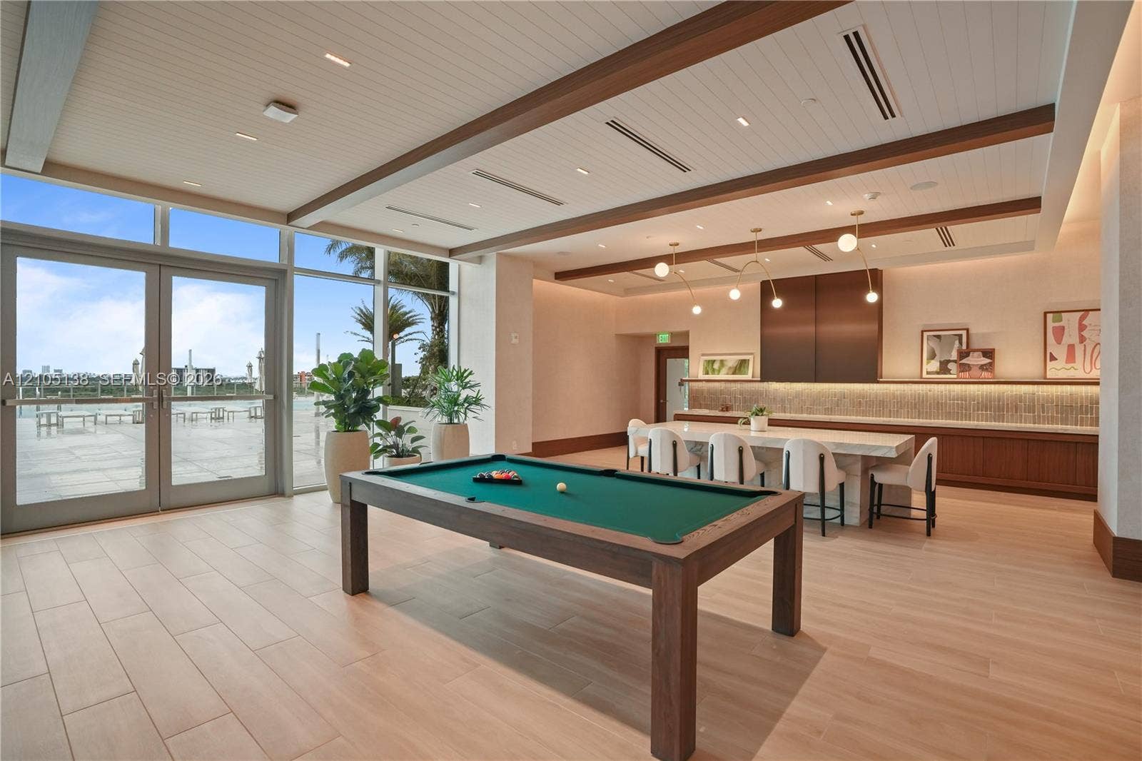 2411 Laguna Circle, #1505, North Miami, FL 33181 Spacious entertainment area with large format tile flooring, a built-in buffet with wood-finish cabinetry, a decorative accent wall, and expansive glass doors opening to an exterior patio