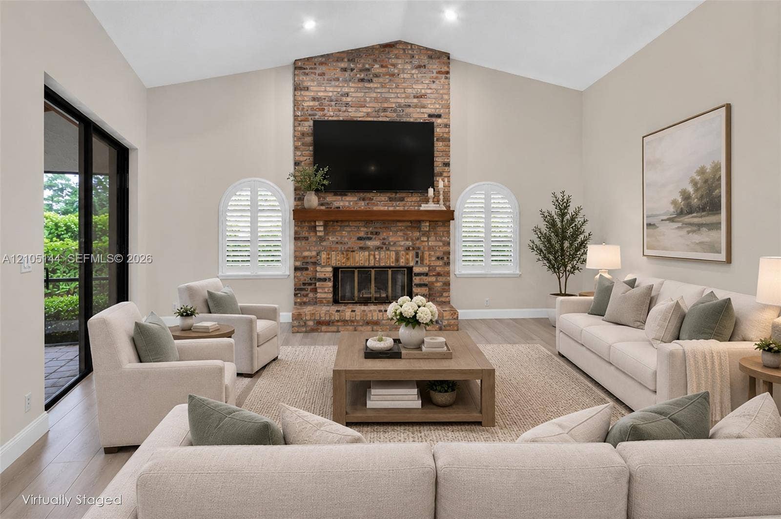 Vaulted ceilings, full-height brick fireplace, wood-finish mantel, arched windows with plantation shutters, and sliding glass doors