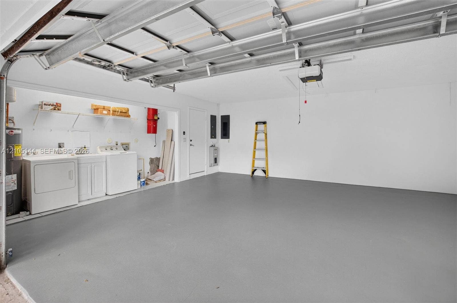 Garage space featuring a smooth epoxy-finish floor, built-in laundry area with utility sink, ceiling-mounted automatic door opener, and white wall finishes