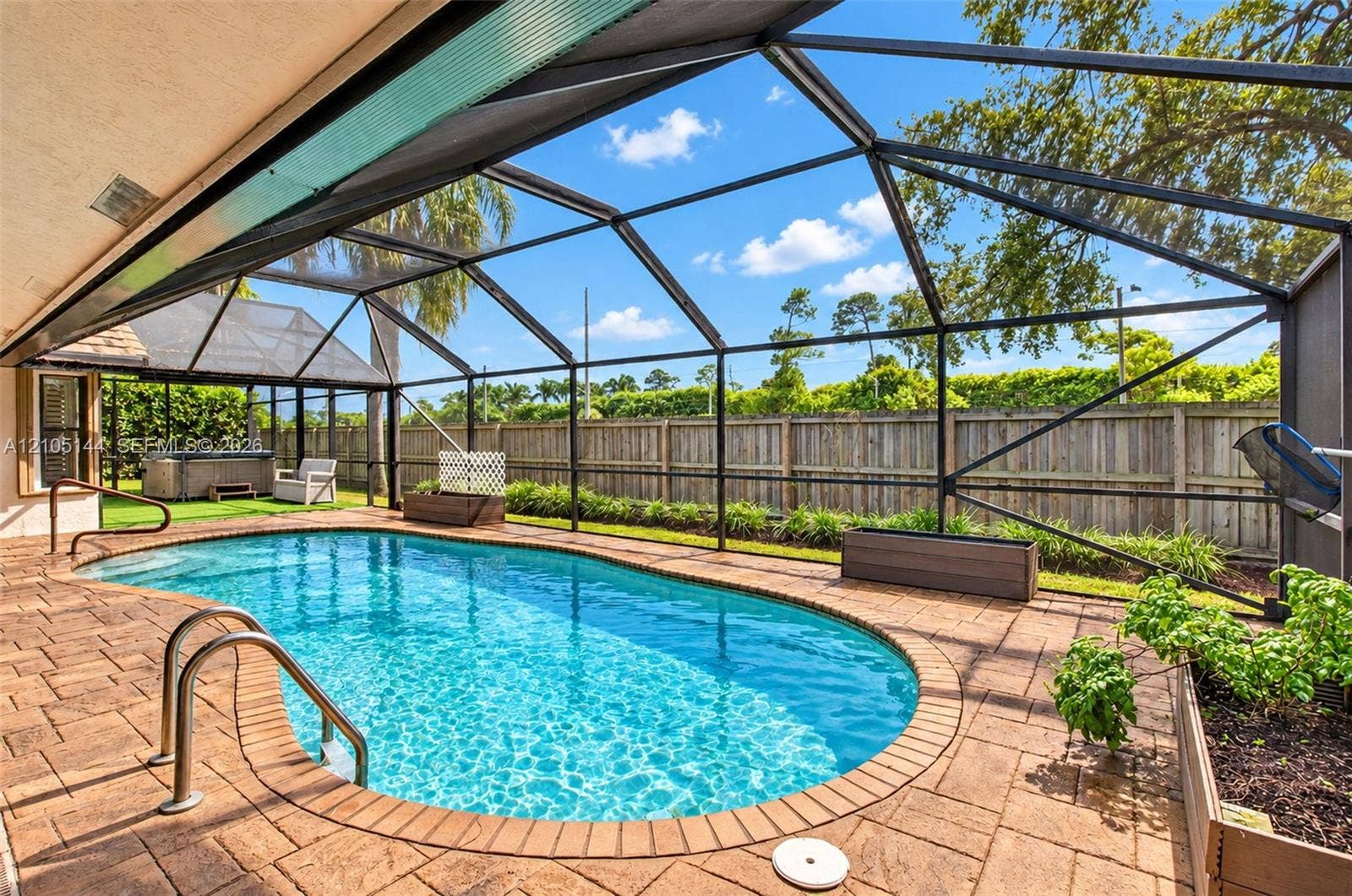 Screened pool enclosure featuring paver decking, stainless steel pool ladder, and wood privacy fencing