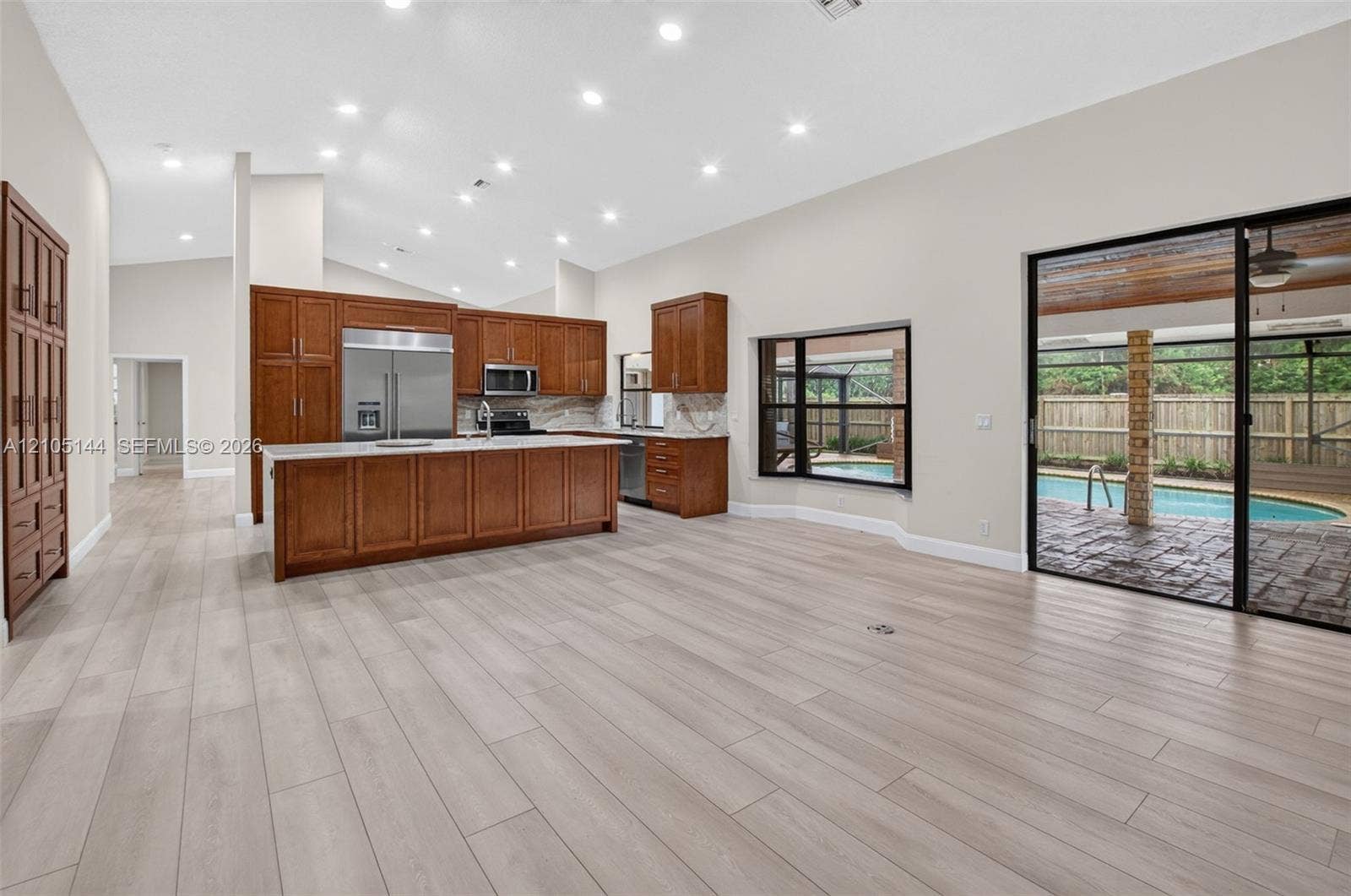Kitchen featuring stained wood cabinetry, stainless steel appliances, and a center island with light-toned countertops, complemented by wood-finish flooring and recessed lighting throughout