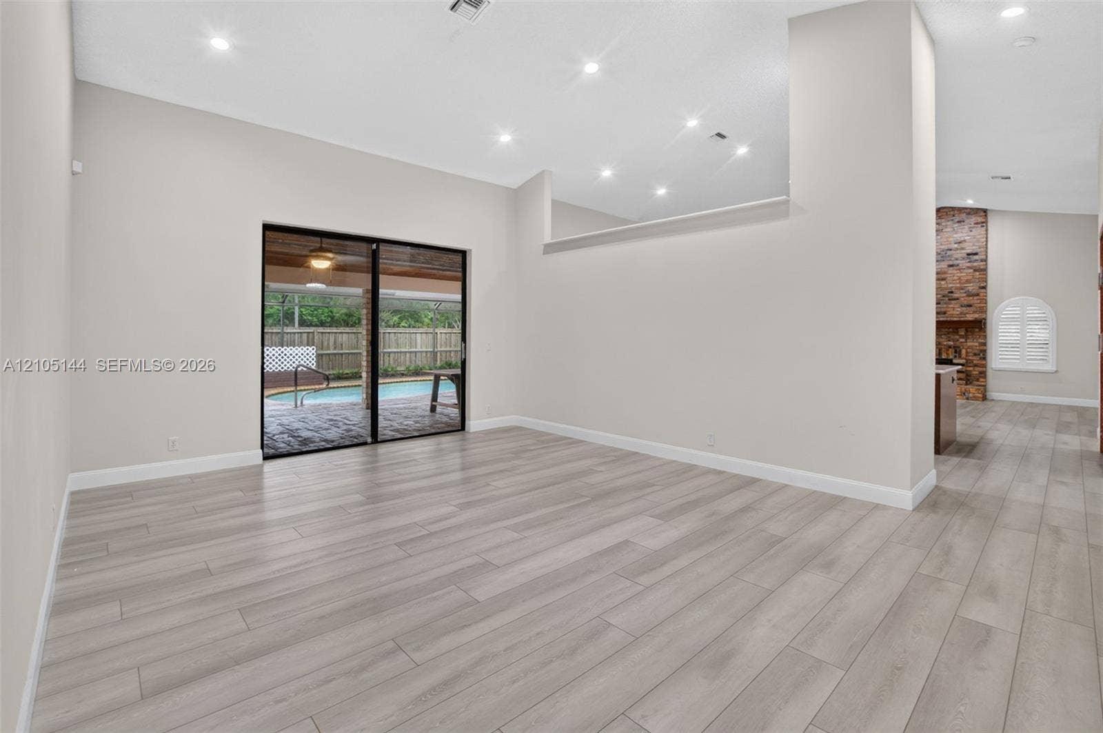 Open living area featuring wood-finish flooring, recessed lighting, high ceilings with architectural cutouts, sliding glass doors, and a brick-accented interior wall