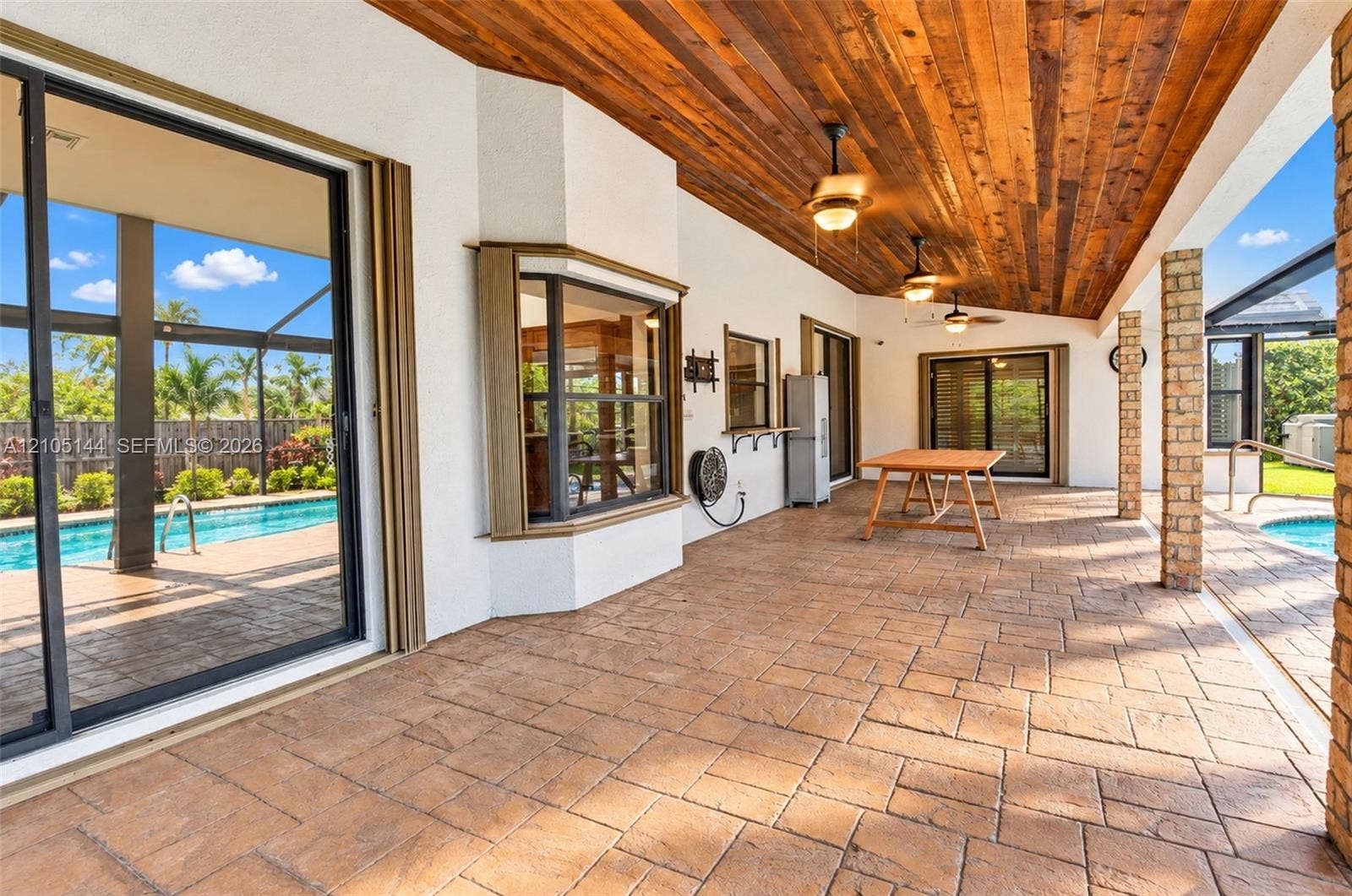 Covered lanai featuring a tongue-and-groove wood ceiling, stamped concrete flooring, brick pillars, and sliding glass door access