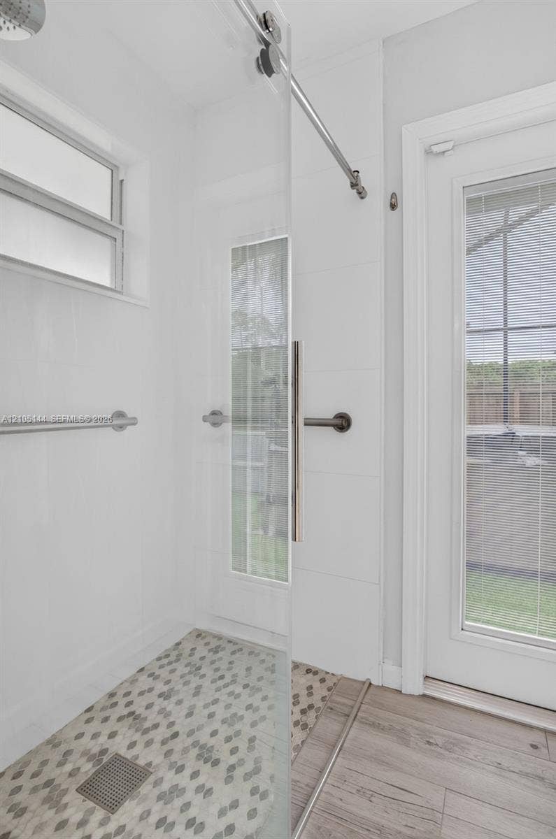 Walk-in shower featuring a sliding glass door, hexagonal tile flooring, wall-mounted brushed metal hardware, and a rainfall shower head