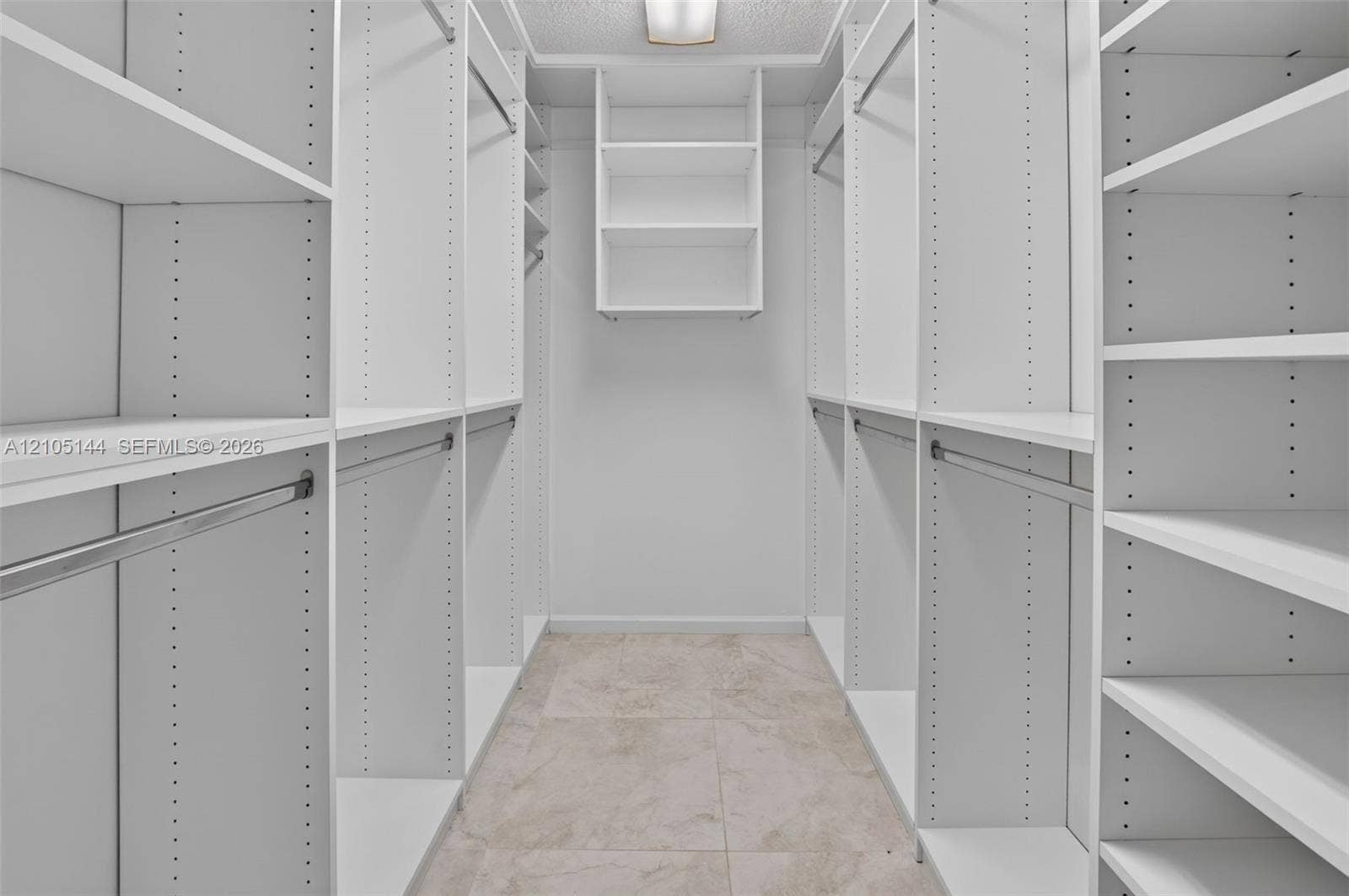 Walk-in closet featuring white built-in shelving, adjustable shelf tracks, metal garment rods, and tile flooring