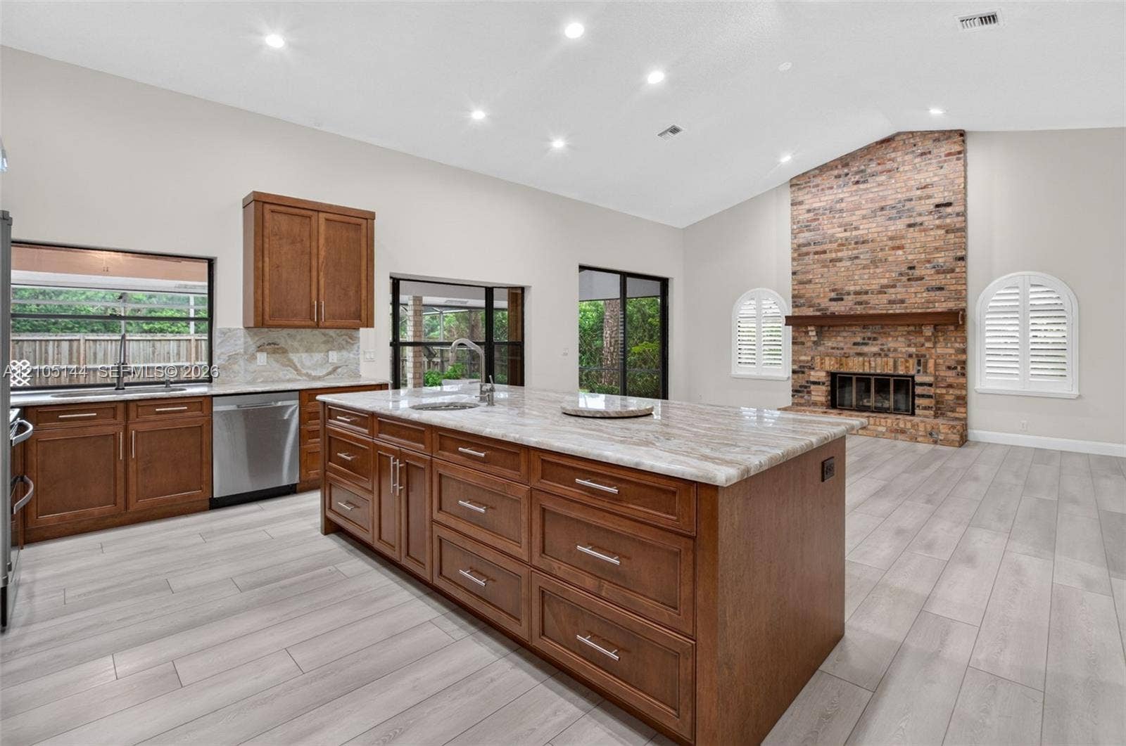Kitchen featuring a central island with a stone countertop, stained wood cabinetry, recessed lighting, wood-finish flooring, and a floor-to-ceiling brick fireplace