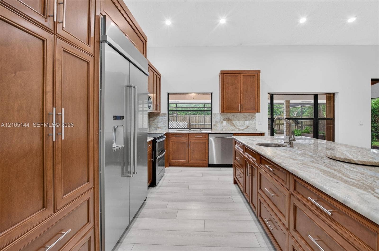 Kitchen featuring wood cabinetry, expansive stone countertops, stainless steel appliances, a center island with a prep sink, and tile flooring