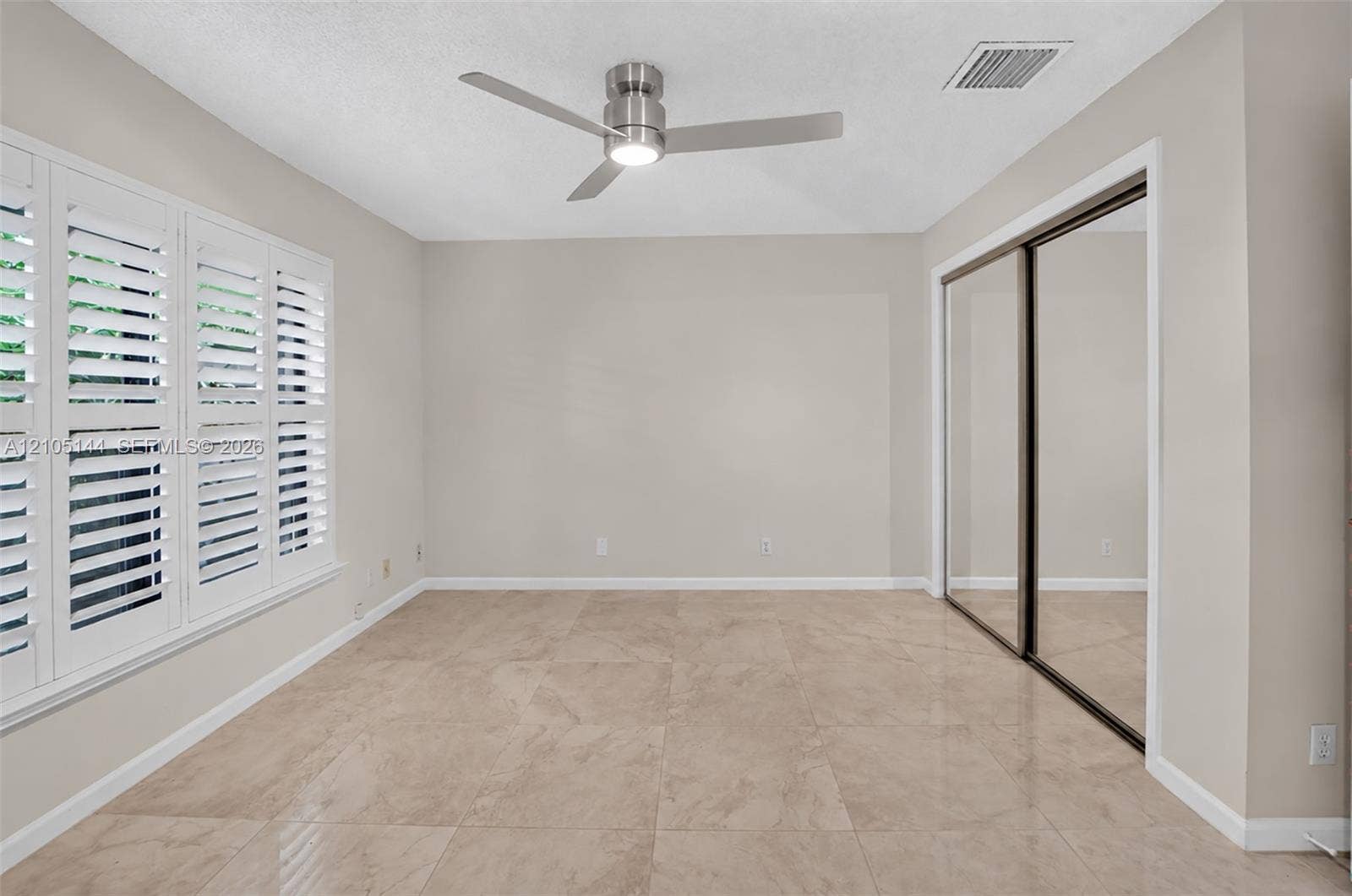 (FAN VIRTUALLY STAGED AS SIMILAR PIECE WILL BE INSTALLED)Large-format tile flooring, multi-panel plantation shutters, ceiling fan with integrated lighting, and floor-to-ceiling mirrored closet doors