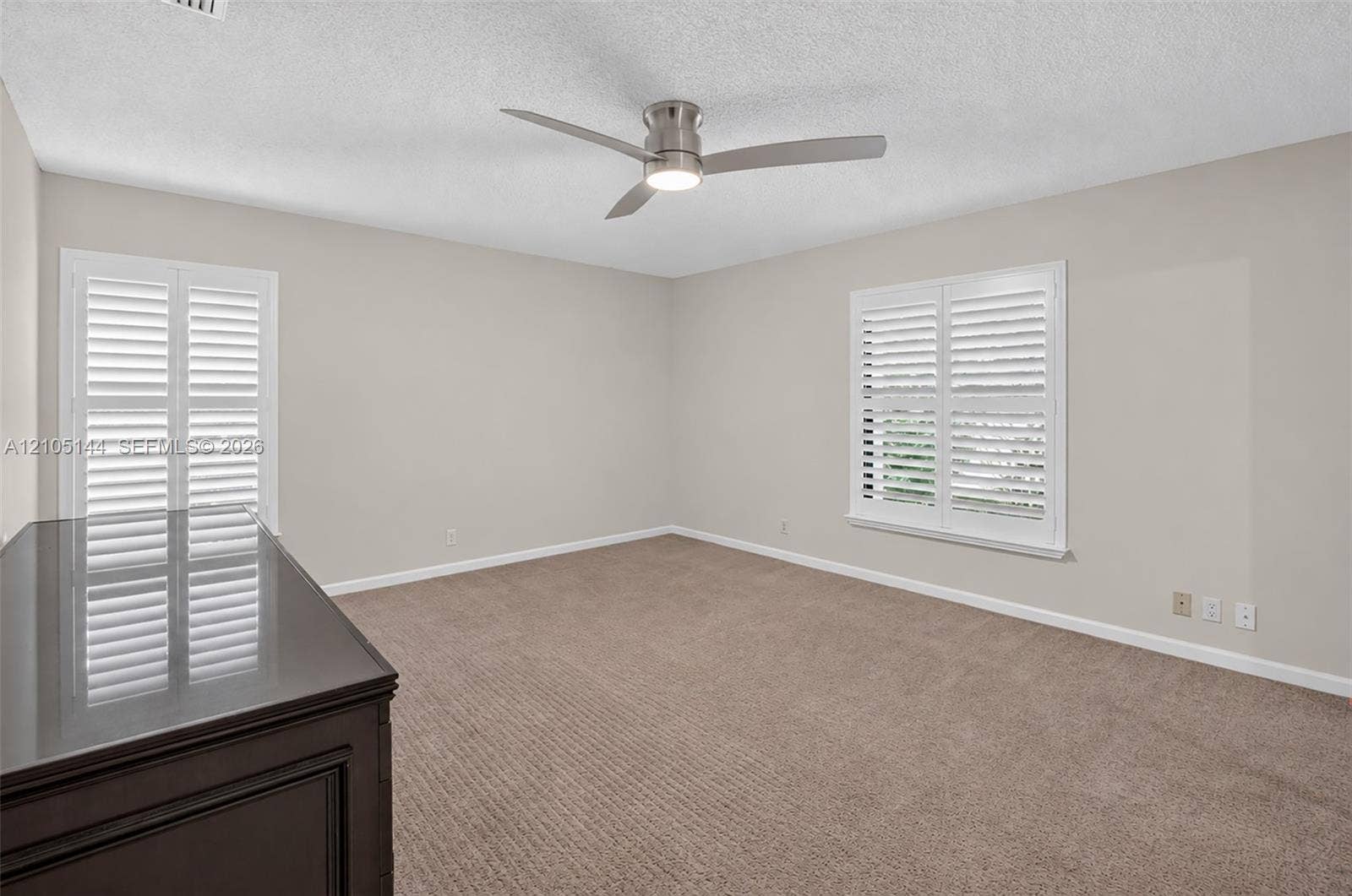 (FAN VIRTUALLY STAGED AS SIMILAR PIECE WILL BE INSTALLED) Neutral-toned interior featuring wall-to-wall carpeting, white plantation shutters, and a modern brushed-nickel ceiling fan with integrated lighting