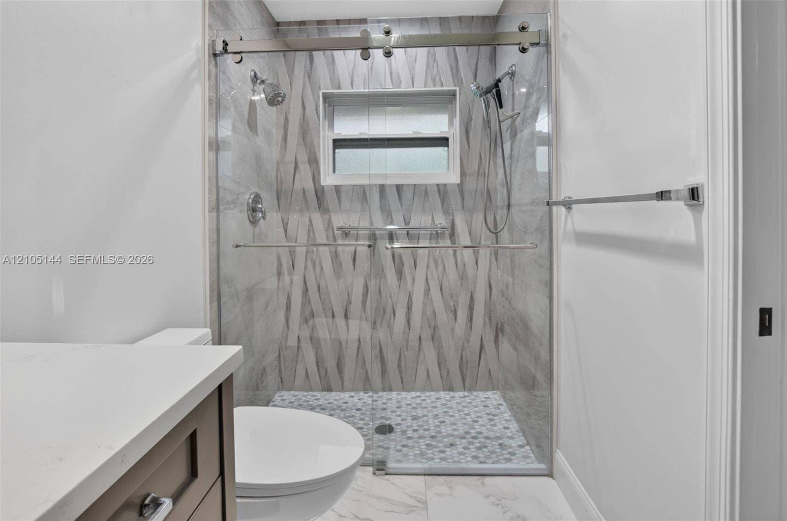 Walk-in shower featuring a sliding glass door, patterned wall tiling, hexagon mosaic floor tiling, dual shower heads, and an integrated window