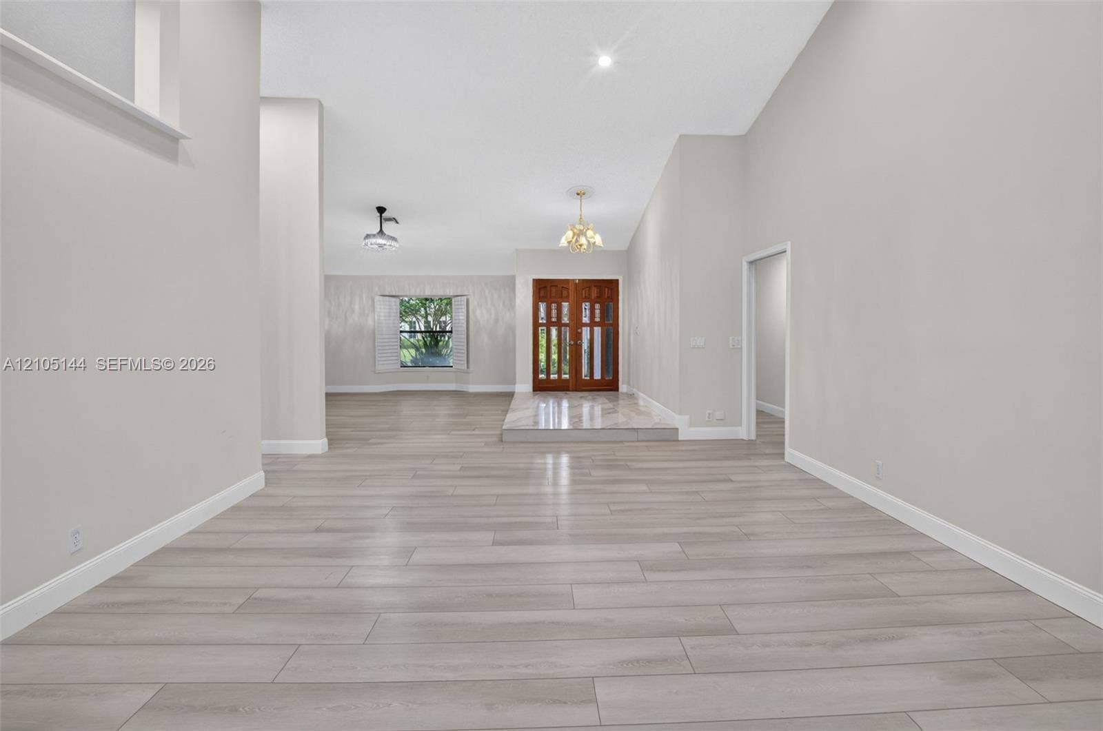 Open interior featuring vaulted ceilings, wood-finish flooring, double-door entryway, elevated stone-finish foyer landing, and a bay window