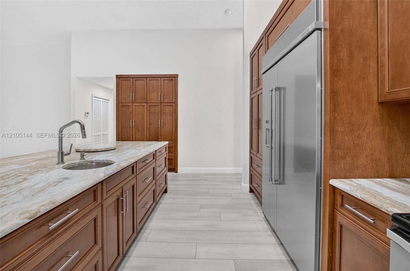 Kitchen featuring wood cabinetry, expansive stone countertops, stainless steel side-by-side refrigerator, under-mount prep sink with high-arc faucet, and large-format tile flooring