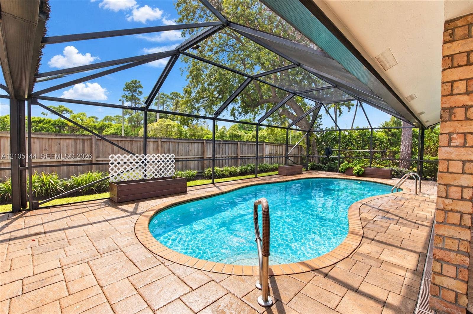 Screened-in pool area featuring a paver deck, brick siding, built-in wooden planters, and a wood privacy fence