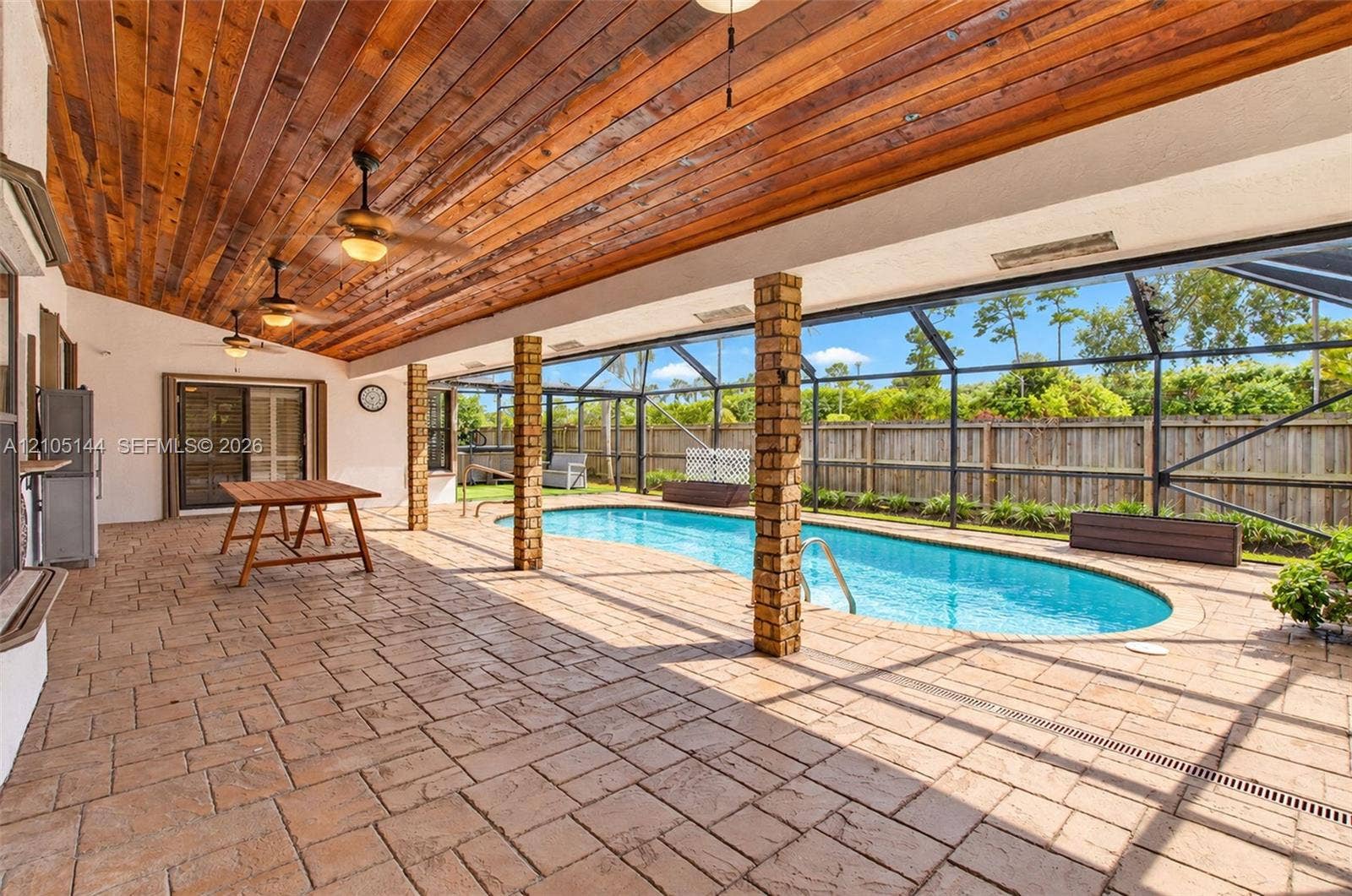 Screened-in pool area featuring a natural wood-plank ceiling, exposed brick columns, and patterned paver patio flooring