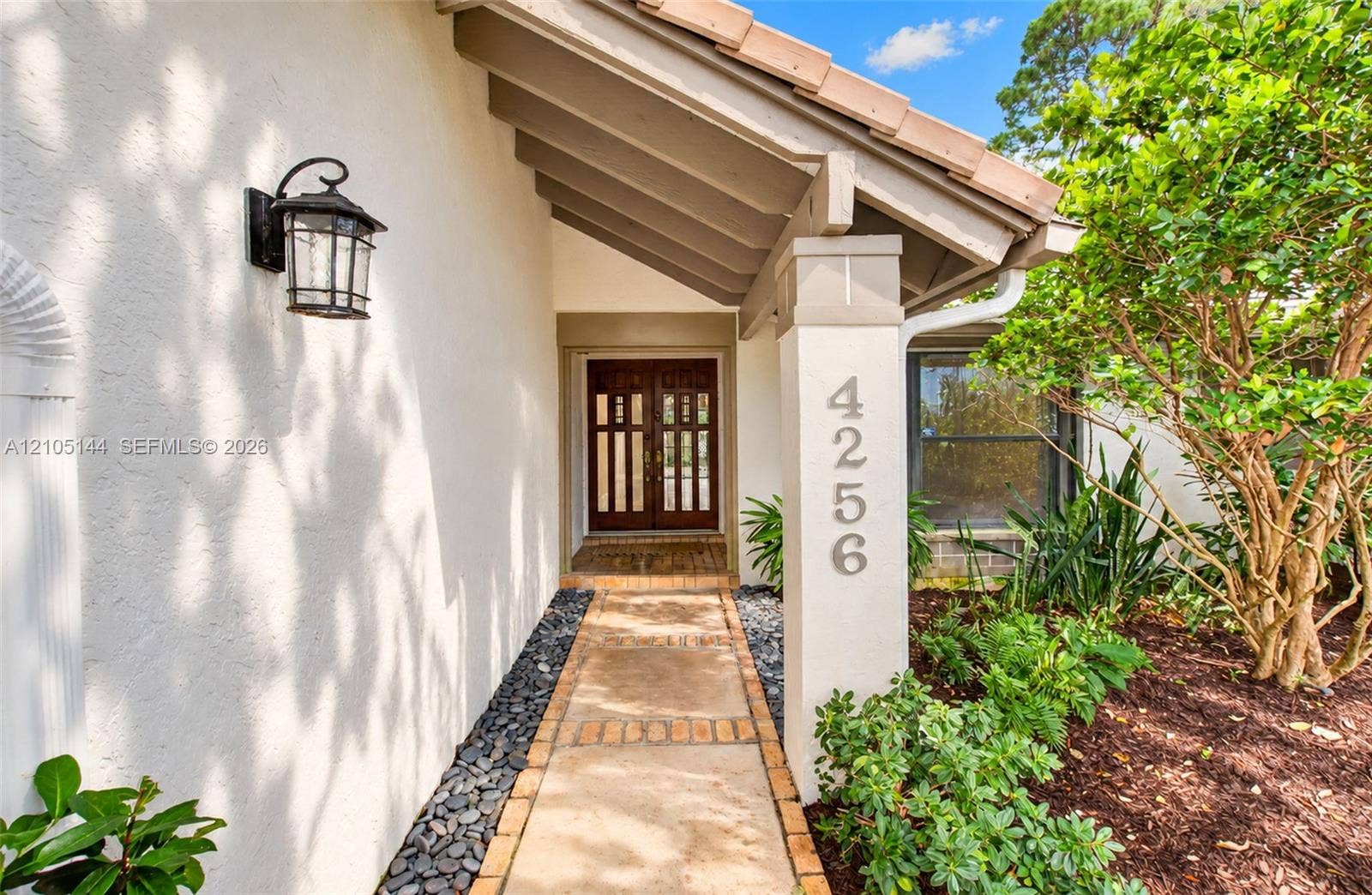 Covered entryway featuring a concrete paver walkway, stucco exterior, decorative wall-mounted light fixture, and double entry doors with vertical glass panes