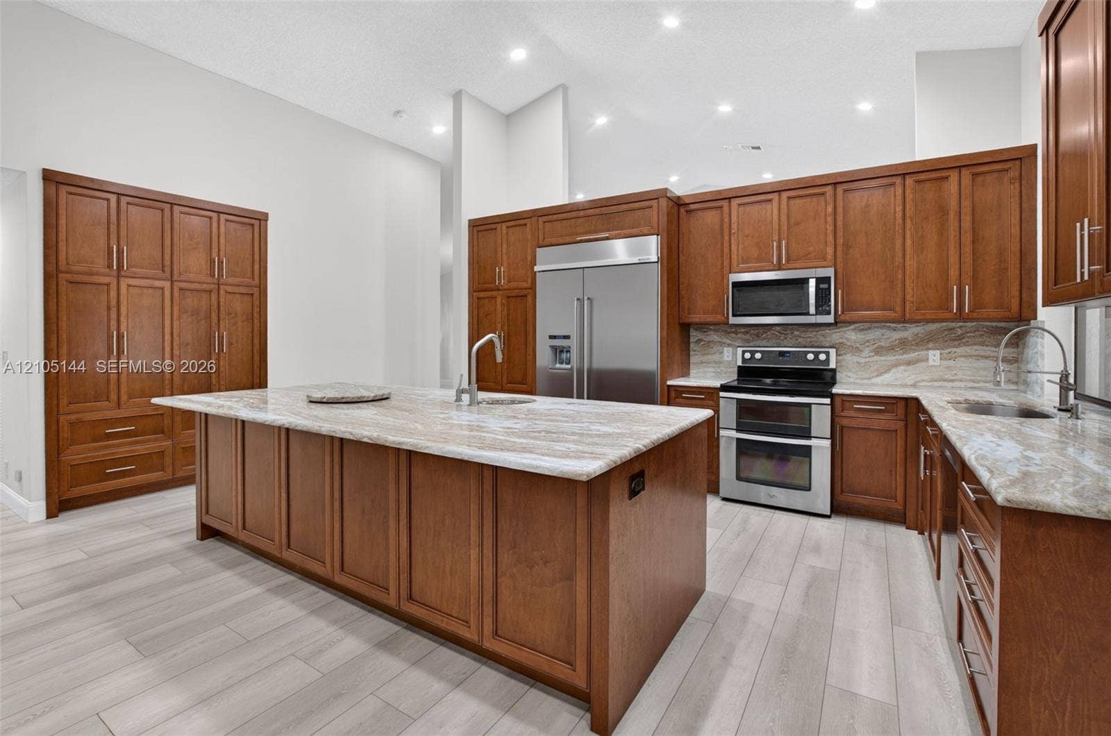 Kitchen featuring wood cabinetry, large central island, stone countertops, stainless steel appliances, and wood-finish flooring