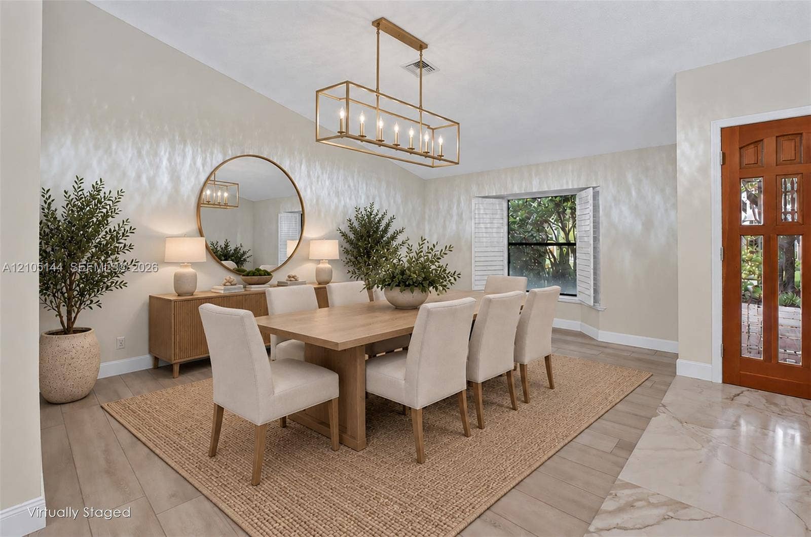 Dining room featuring wood-finish flooring, a contemporary rectangular chandelier, a large round wall mirror, and a wood-paneled door with glass inserts