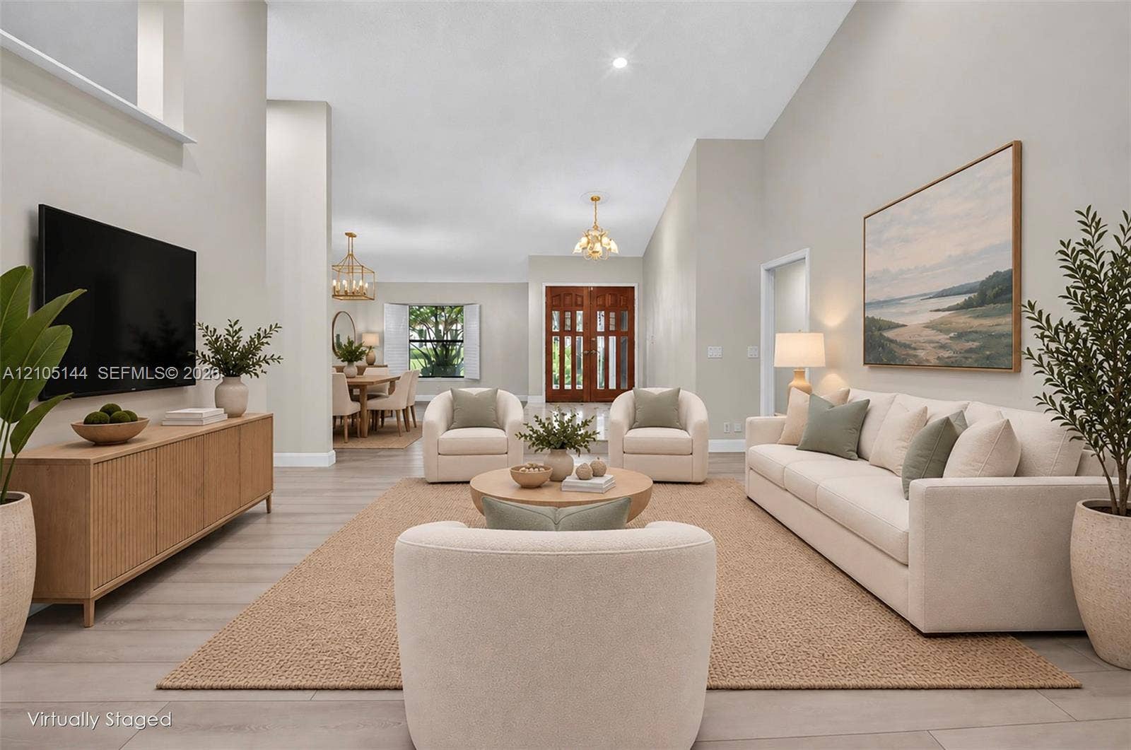 Spacious interior featuring vaulted ceilings, neutral wall tones, light wood-finish flooring, double front entry doors with glass panels, and multiple hanging pendant light fixtures