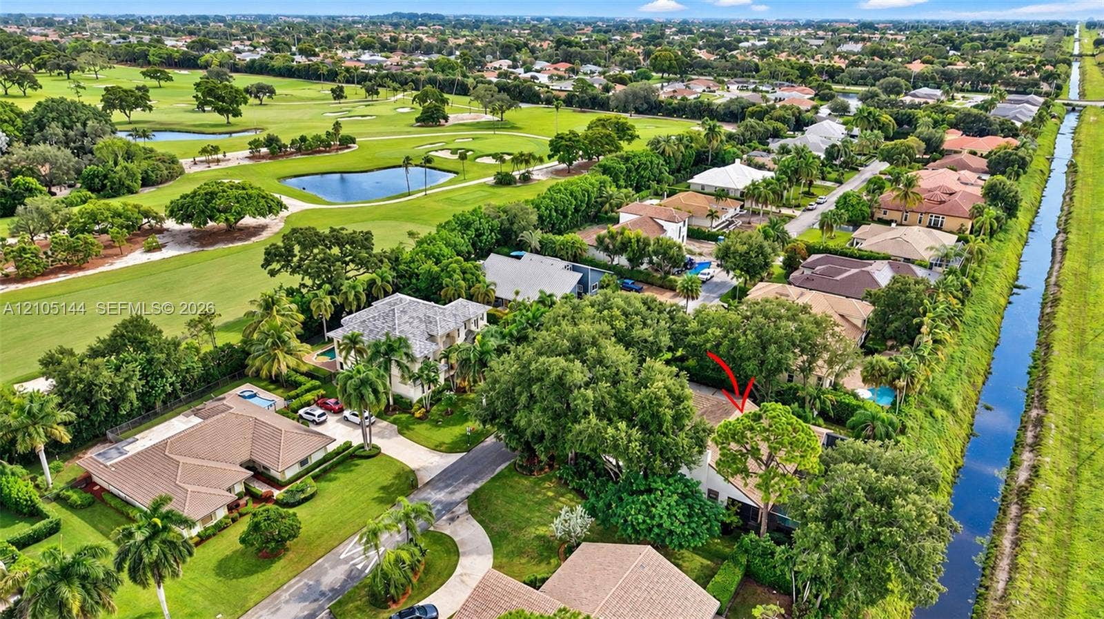 Aerial perspective of property featuring mature canopy trees, tiled roofing, and proximity to canal waterways and golf course grounds