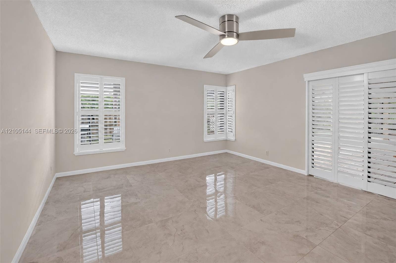 (FAN VIRTUALLY STAGED AS SIMILAR PIECE WILL BE INSTALLED)Large-format neutral tile flooring, triple white plantation shutters, and a modern brushed-nickel ceiling fan with integrated lighting