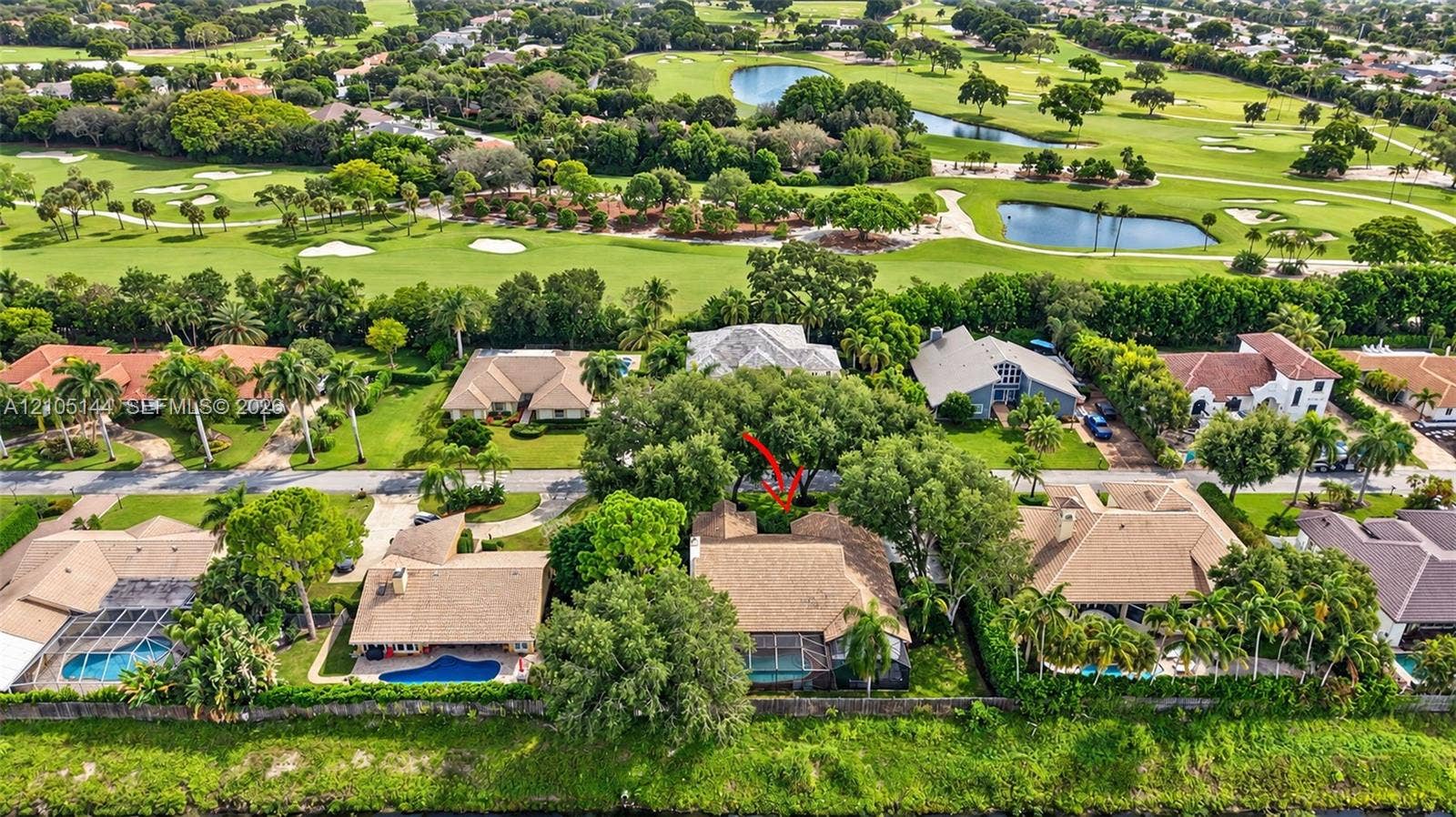 Aerial perspective showcasing a residential property with a shingle roof and a screened-in lanai, situated on a golf course lot featuring mature trees and waterfront elements