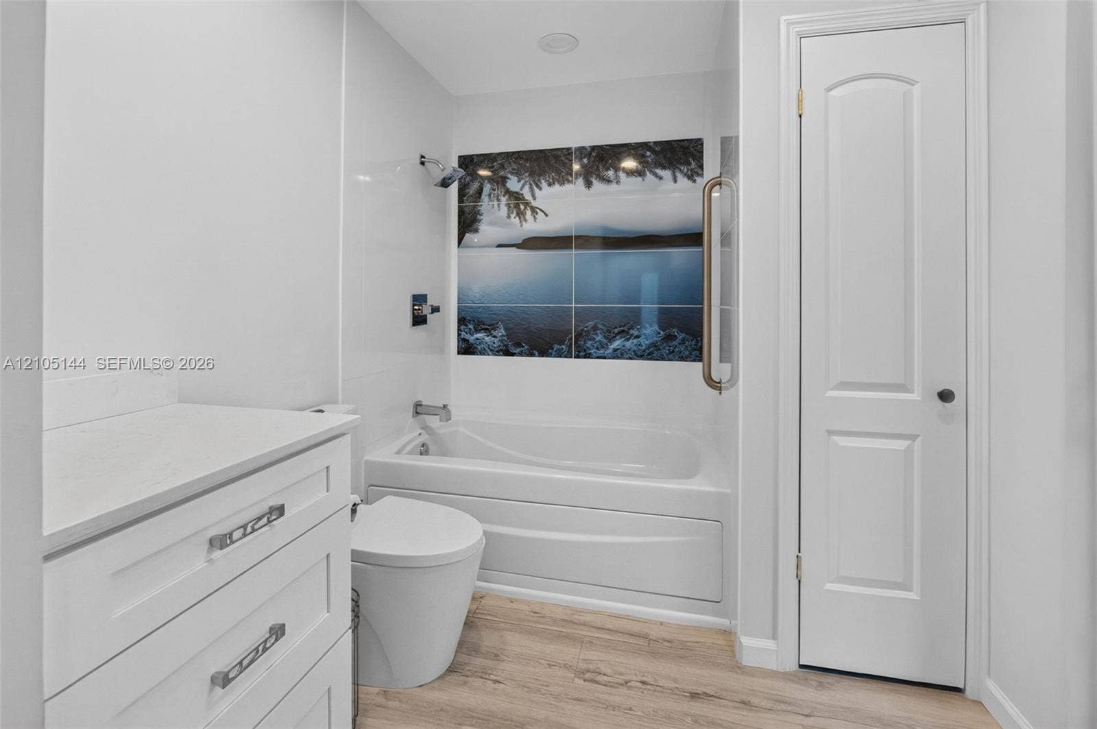 Bathroom featuring white cabinetry with stone-finish countertop, wood-finish flooring, a built-in soaking tub, decorative wall tile inlay, and a wall-mounted grab bar